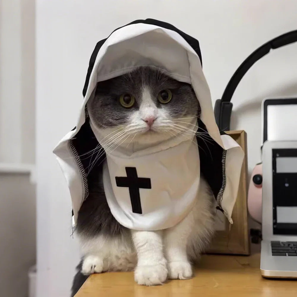 A gray cat wearing a white nun costume with a black cross on its face, sitting on a wooden surface.
