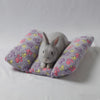 A gray plush rabbit sits on a purple star-patterned pillow for a pet bed.
