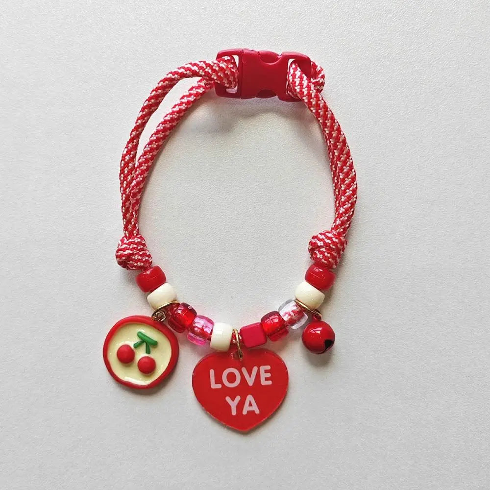 A red braided pet collar with a bell and a heart-shaped tag featuring red berries.