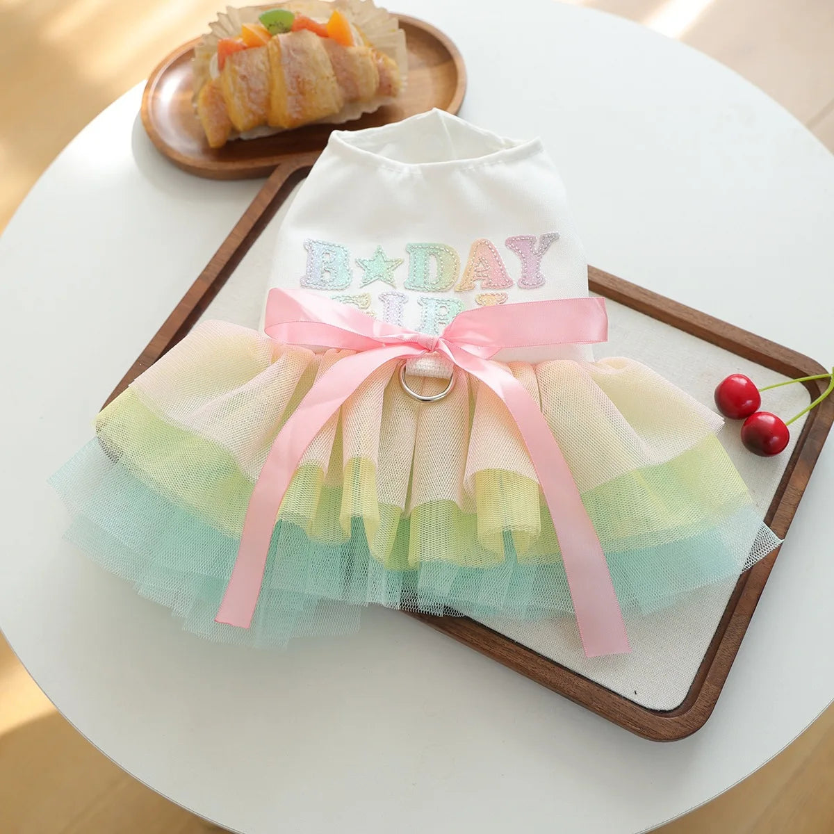 A white and pink elegant birthday suit for a small puppy with a tulle skirt and bow, displayed on a wooden tray.
