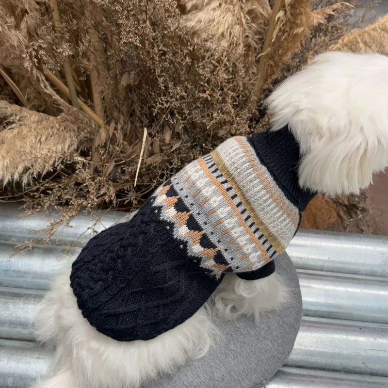 A black plaid knit sweater for dogs with white fluffy trim, resting against dried natural grasses.