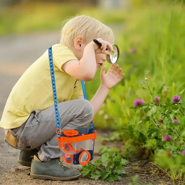 A young child is observing insects in a garden using an insect observation box with dual magnifiers.
