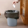 A hand is lowering a white plastic tie handle into a dark gray disposable garbage bag.