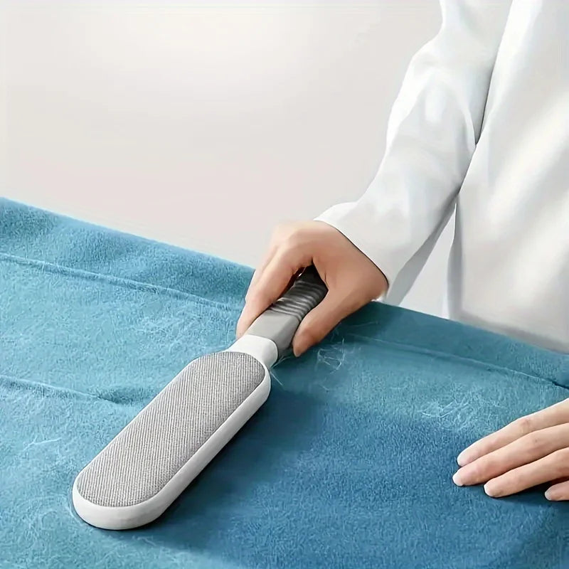 Une main utilise une brosse à poils pour enlever les poils d'animaux grise sur un tissu bleu.