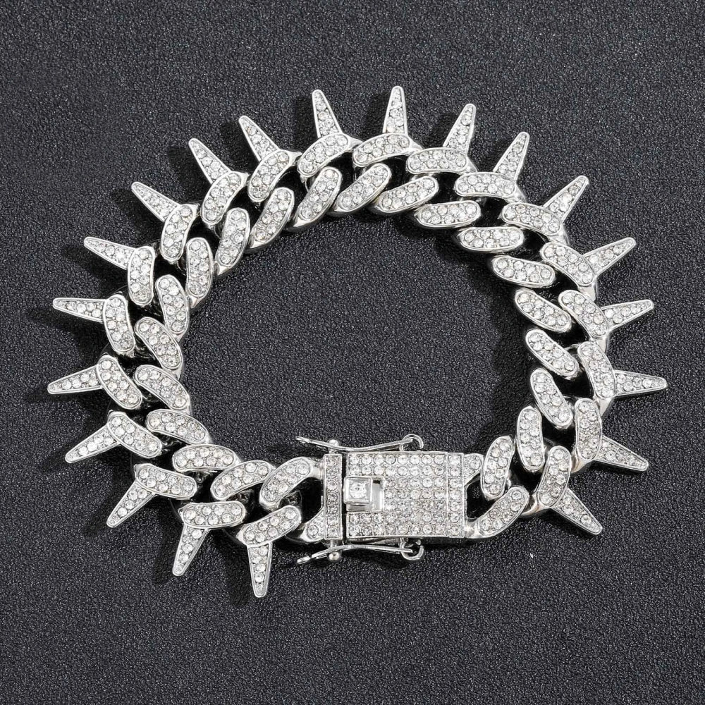 A silver spiked Cuban chain bracelet adorned with diamond accents, displayed against a dark background.