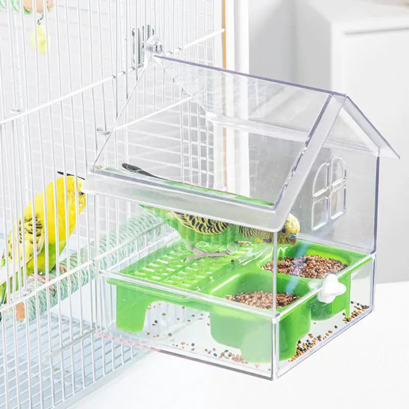 A clear plastic parrot feeder and bird bath accessory with a green tray for feeding birds inside a wire cage.