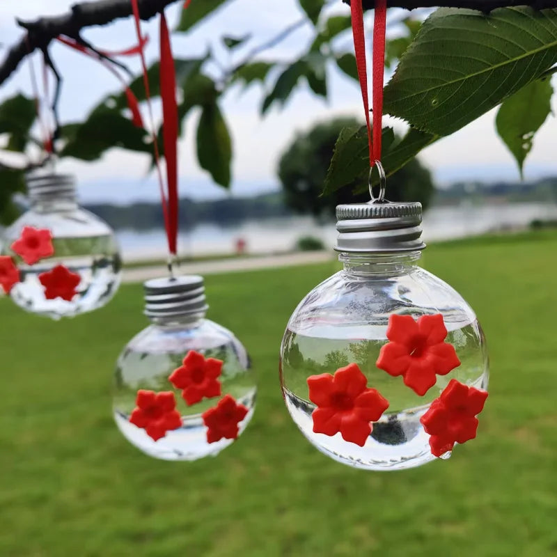 A glass bottle filled with water and red flowers hangs from a branch in an outdoor setting.