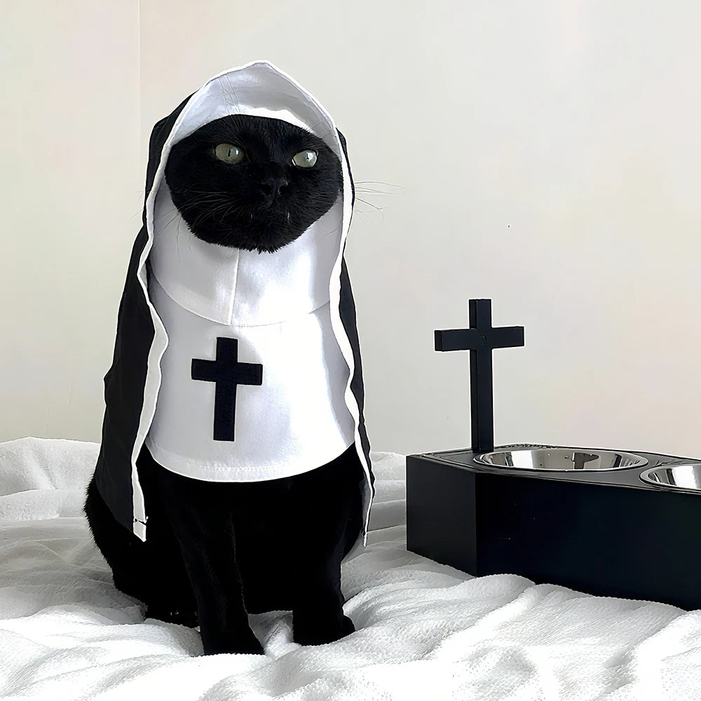 A black cat dressed in a white nun costume with a black hood sitting on a white blanket.