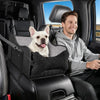 A smiling man sits in a car seat with a small white dog resting on the seat.