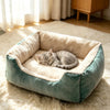 A gray cat is sleeping inside a plush teal pet bed with a fluffy cream lining on a light rug.