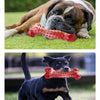 A brown and white dog is lying down with a red rubber chew toy for teeth cleaning next to it.