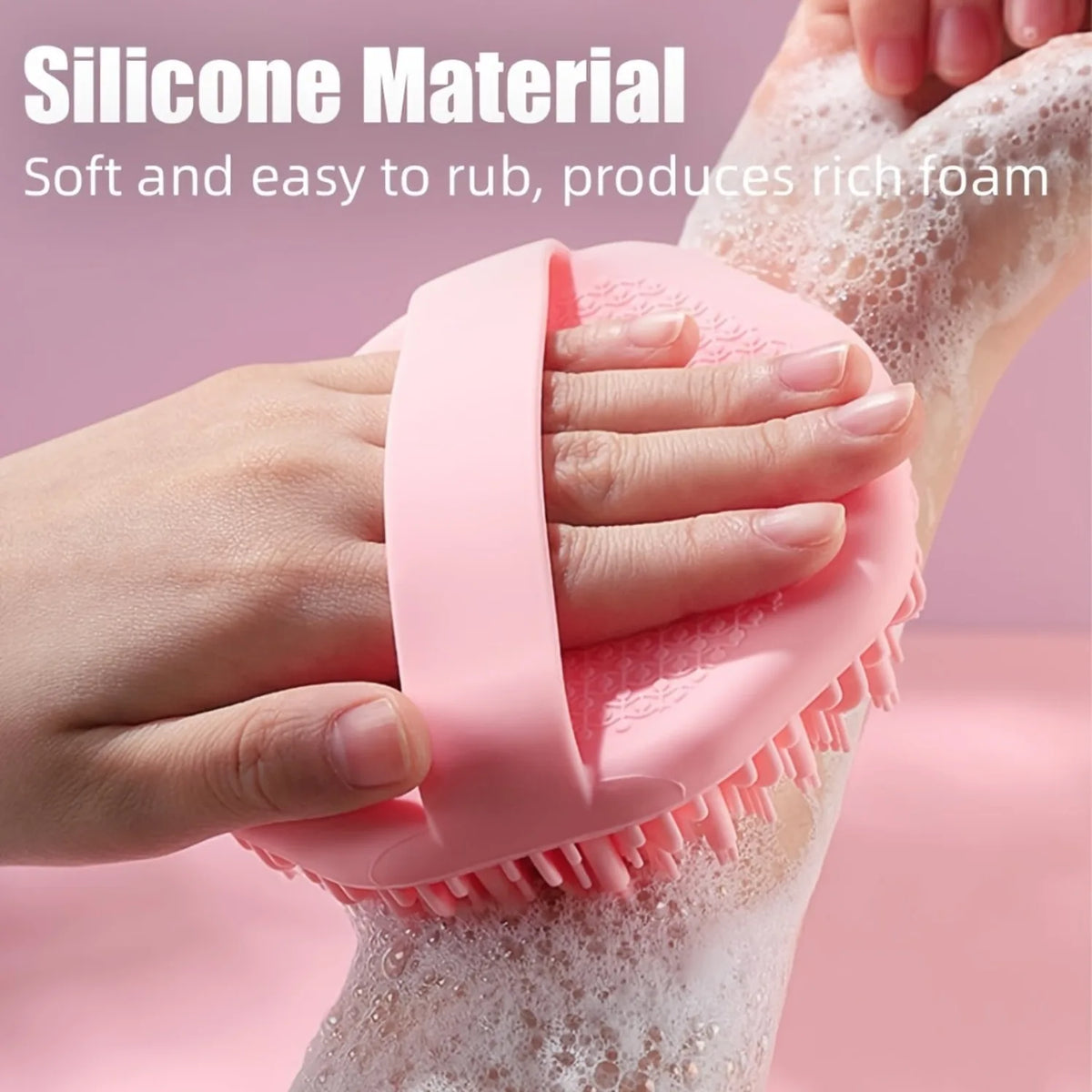 A hand is using a pink silicone exfoliating brush on a person's leg, creating rich foam.