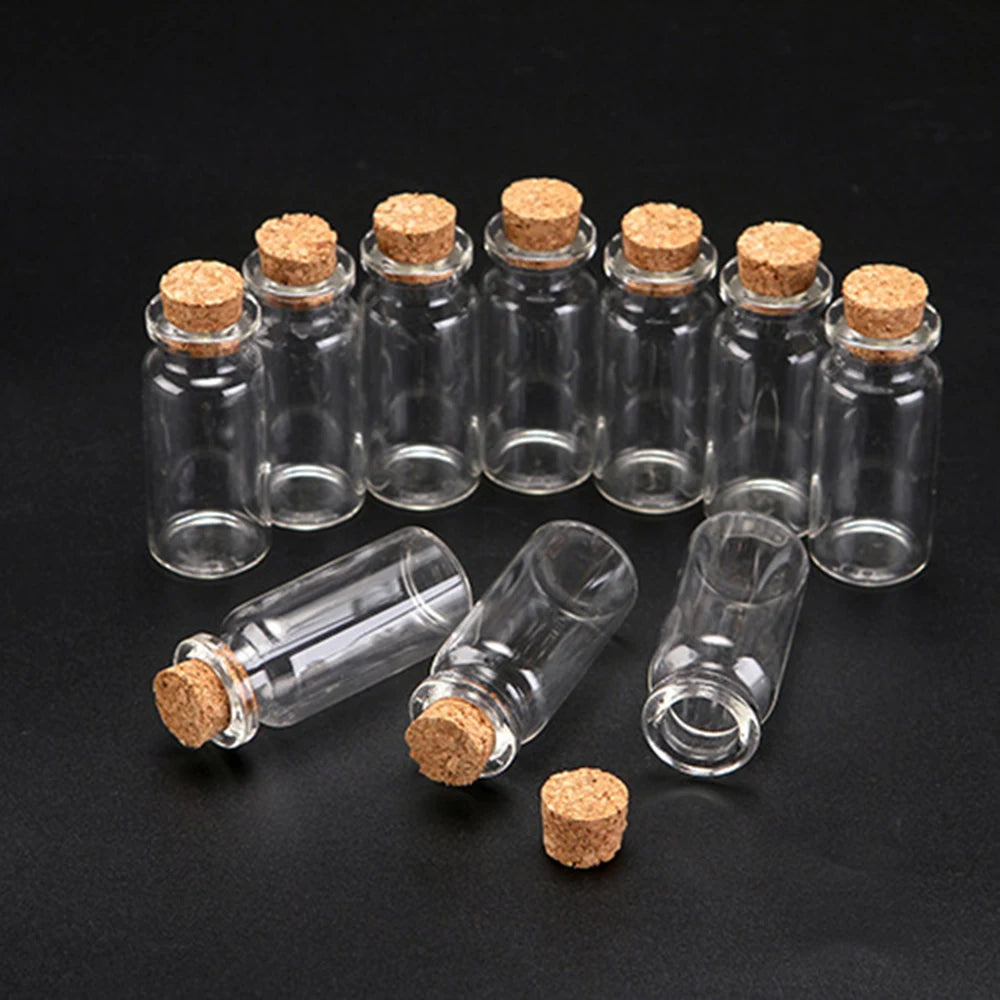 A collection of ten mini glass bottles with cork stoppers arranged on a dark surface.