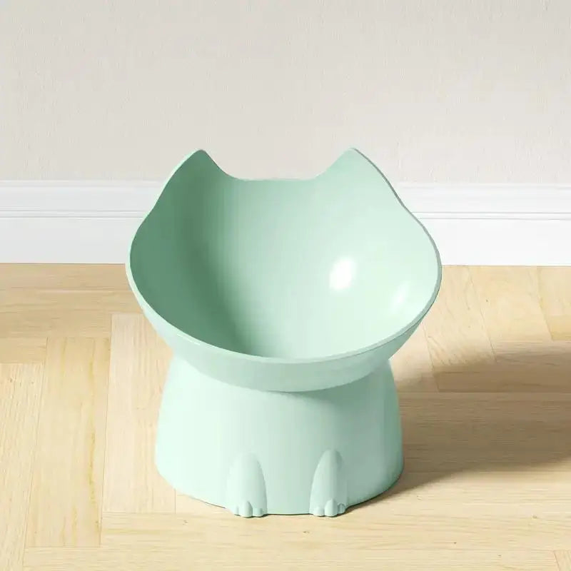 A light mint green elevated cat bowl with a matching anti-tip base sitting on a wooden floor.