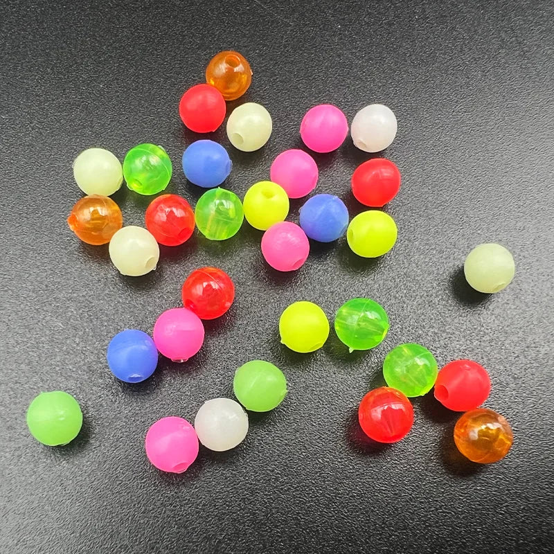 A collection of mixed glow-in-the-dark fishing beads in various bright colors scattered on a dark surface.