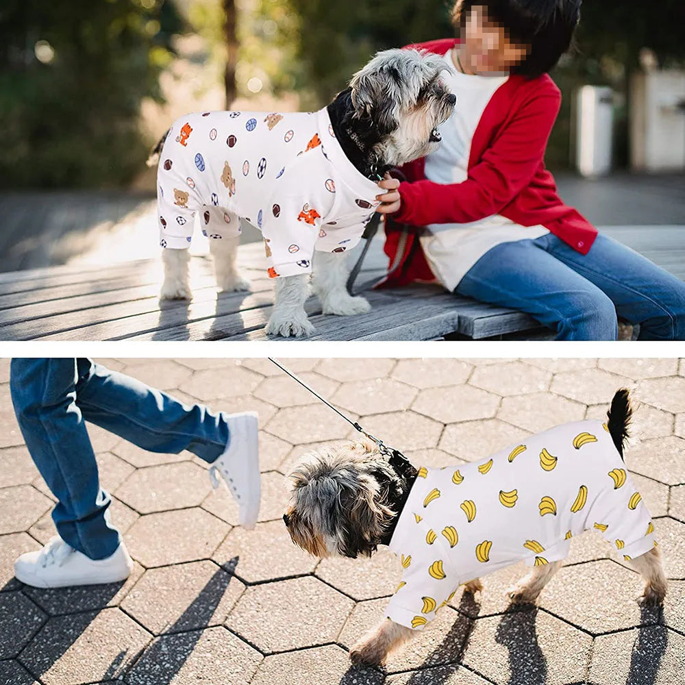 A dog wearing a white patterned cotton pajama is sitting on a wooden deck.