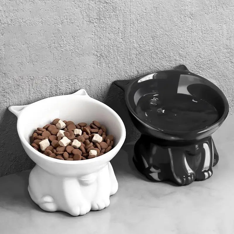 A white elevated slanted cat bowl with an anti-tip base and a black food dish sitting on a gray surface.