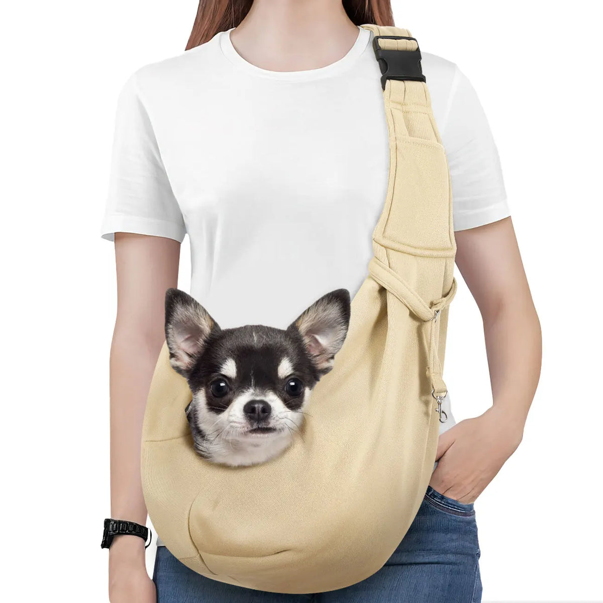 A light beige dog sling carrier with a black strap is worn by a person, featuring a small dog peeking out.