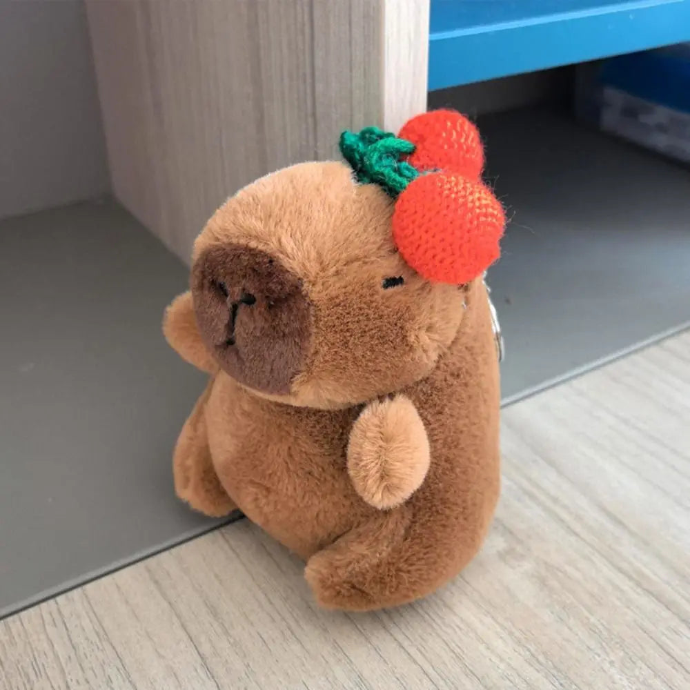 Braune Capybara-Plüschpuppe mit grünen Blättern und orangefarbenen Flügeln auf einer hellen Holzoberfläche.