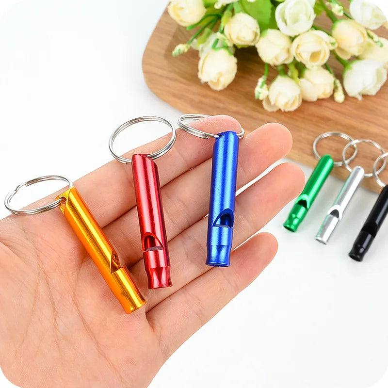 A hand holds several colorful parrot training whistles with metal rings on a wooden surface.
