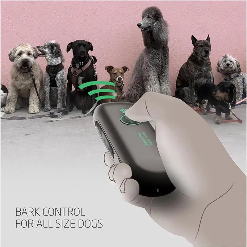 Eine Hand hält ein schwarzes Ultraschall-Hundbell zur Abschreckung vor mehreren Hunden.