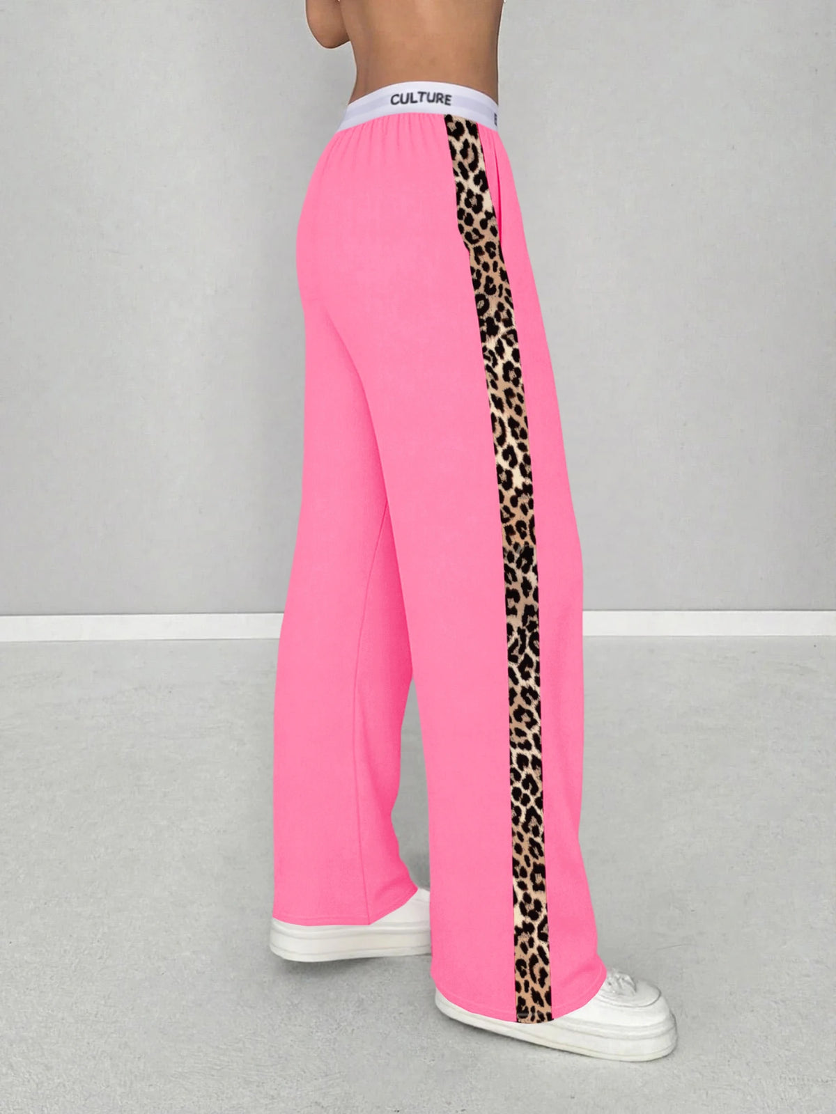 A woman wearing bright pink leopard print high-waist wide leg pants and a white stripe top.