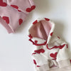 Weißer Hoodie mit roten Herzdrucken und pinken Akzenten, gefaltet auf weißem Untergrund.
