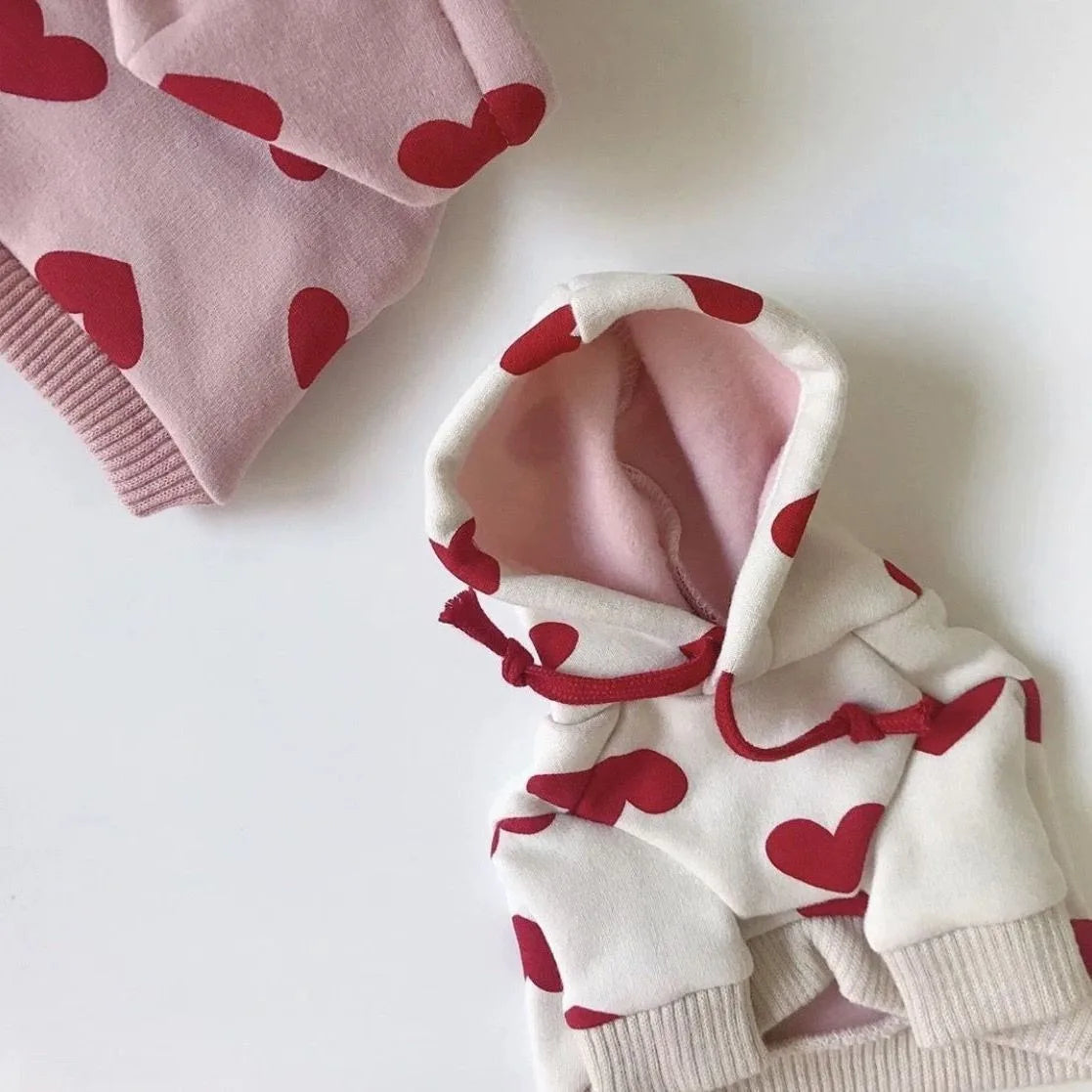 Weißer Hoodie mit roten Herzdrucken und pinken Akzenten, gefaltet auf weißem Untergrund.