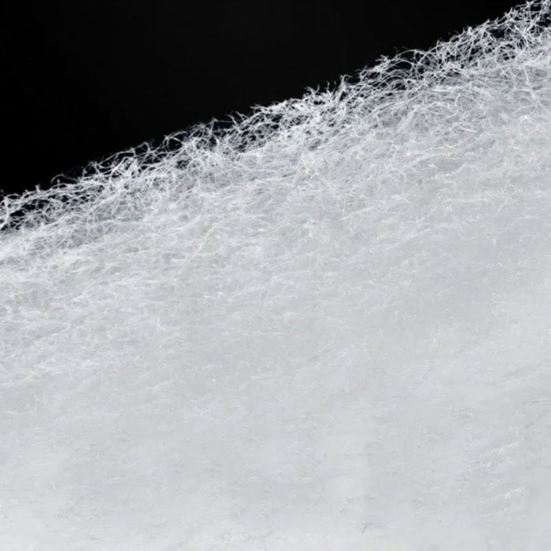 Close-up view of a white, porous filter sponge with fine, fibrous structures against a black background.