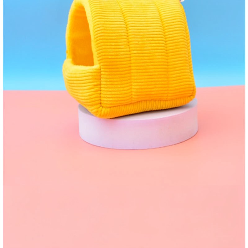 A bright yellow, knitted bird hammock nest resting on a light pink circular stand.
