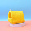 A bright yellow, knitted bird hammock nest is displayed on a white stand against a light blue background.