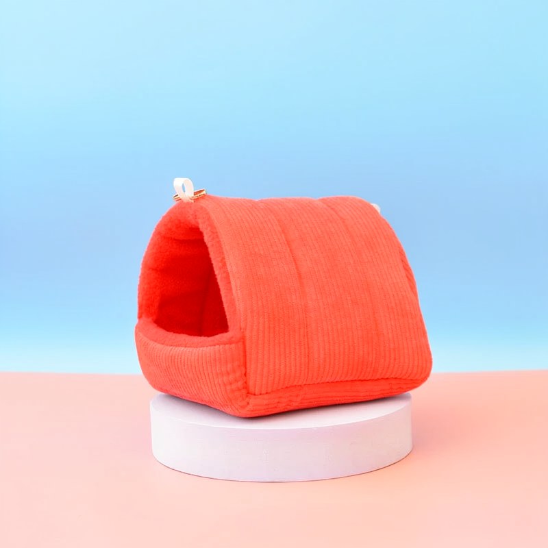 An orange, ribbed cotton bird hammock nest resting on a white circular stand.