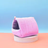 A pink, quilted cotton bird hammock nest is displayed on a light wooden surface against a soft blue background.