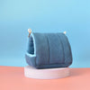 A soft, blue knitted bird hammock nest resting on a white circular stand.