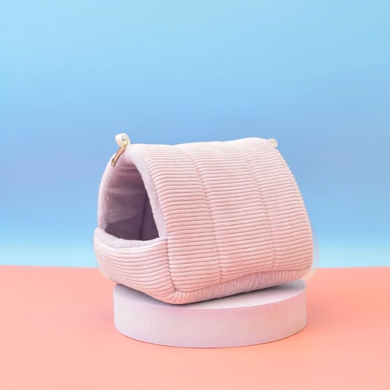 A soft pink cozy cotton bird hammock nest resting on a light pink circular stand.