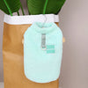 Chaleco de peluche de color verde menta claro y coral, colgado en percha de madera dentro de una bolsa de papel marrón.