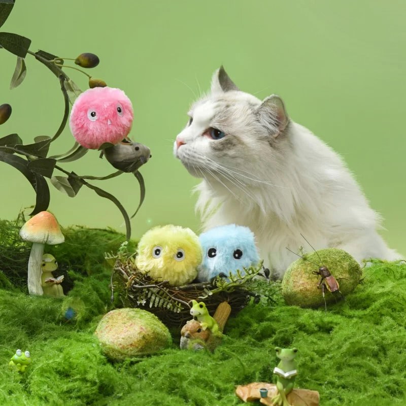 Ein flauschiger weißer Katzenspielball umgeben von Moos, Pilzen und kleinen grünen Kreaturen.