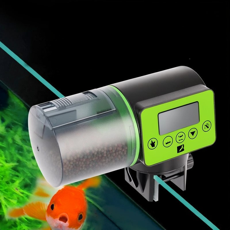 A silver and green automatic aquarium fish feeder device is shown with an orange fish in the background.