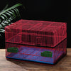 A red mesh bird cage cover with a blue base and green nesting boxes is displayed on a wooden surface.