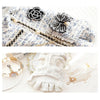 Robe en dentelle blanche ornée de broderies florales noires et de détails dorés, présentée sur fond blanc.