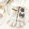 Robe tricotée blanche avec bordure de dentelle et détails de perles, à côté d'une couronne dorée et de branches florales déli