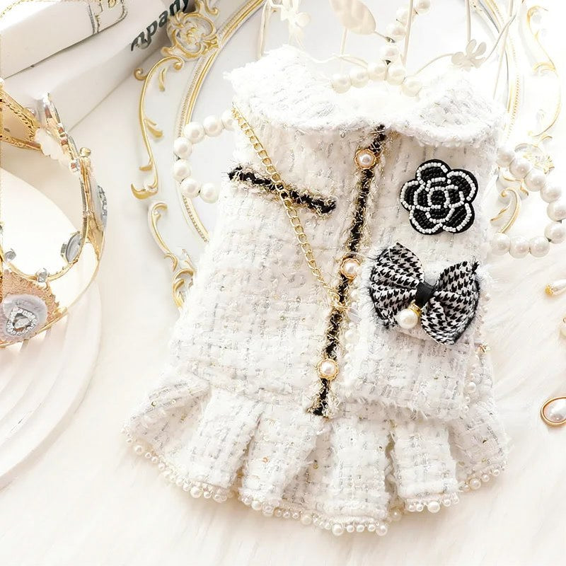 Robe tricotée blanche avec bordure de dentelle et détails de perles, à côté d'une couronne dorée et de branches florales déli